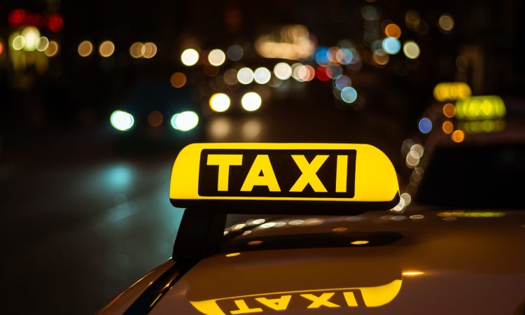 A yellow and black sign of Taxi placed on top of a car at night